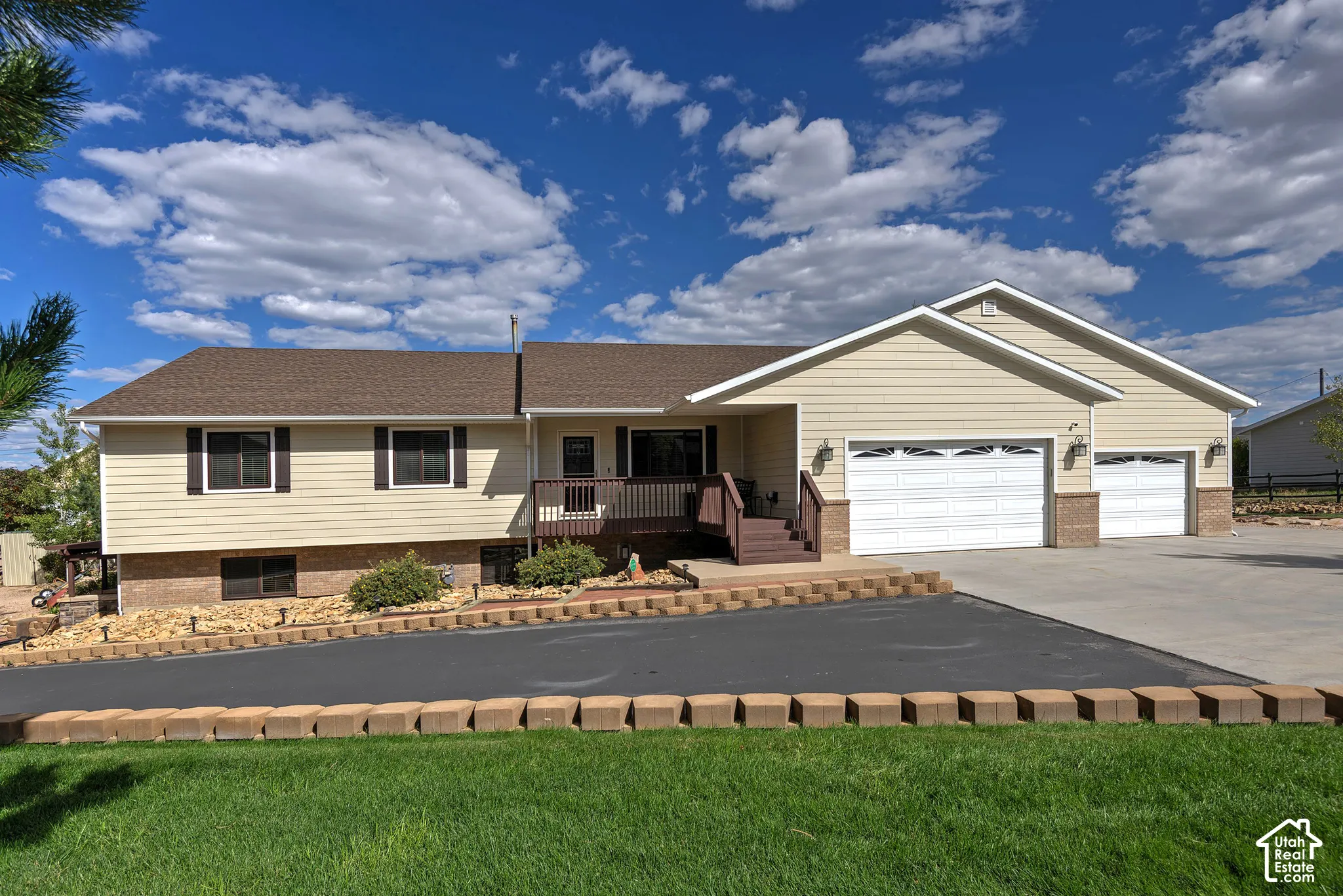 Light-toned siding exterior with brown roof, attached three-car garage, and landscaped front yard with a paved driveway