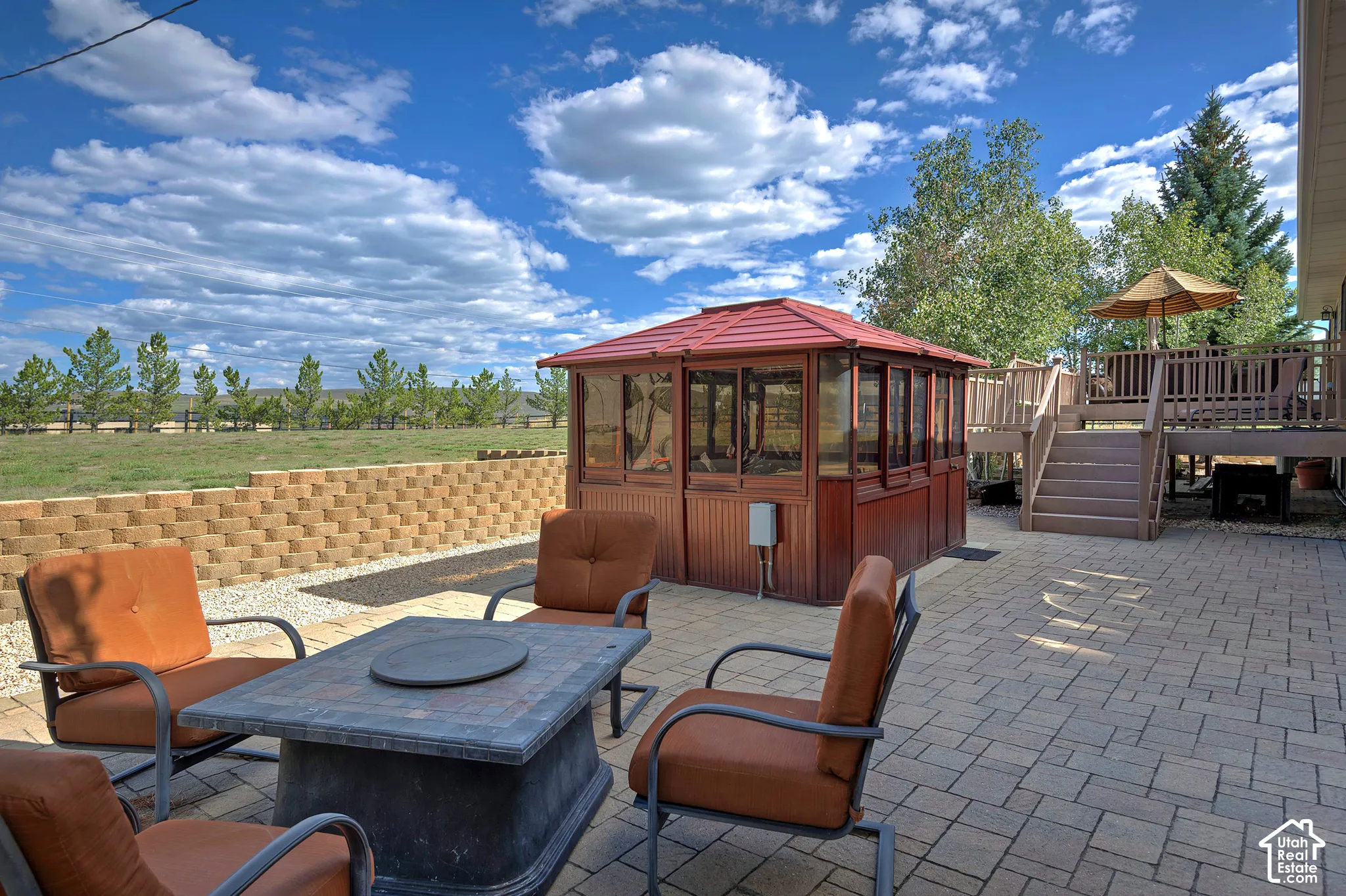 Paver patio with a stone retaining wall, an elevated wood-tone deck, and a wood-toned enclosed spa structure