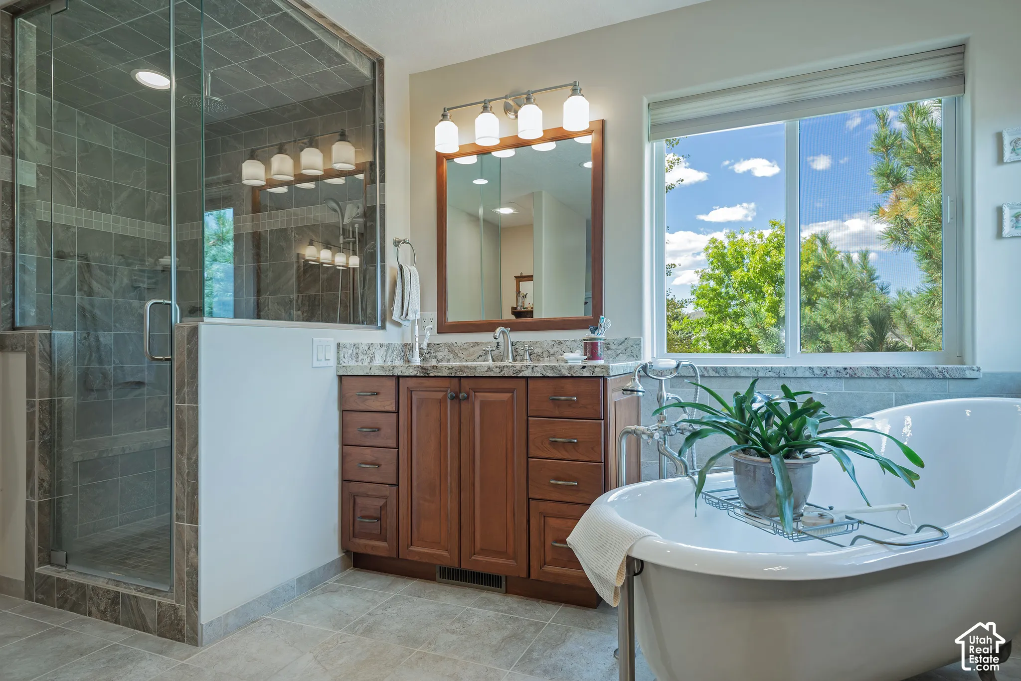 Walk-in shower with glass enclosure, freestanding soaking tub, wood-finish vanity with stone countertop, and large window