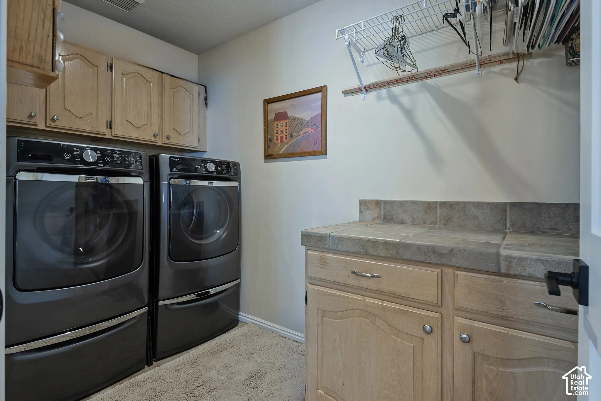 Dedicated laundry area featuring a tile-top countertop, light wood-finish cabinetry with silver hardware, and an integrated wire shelving system