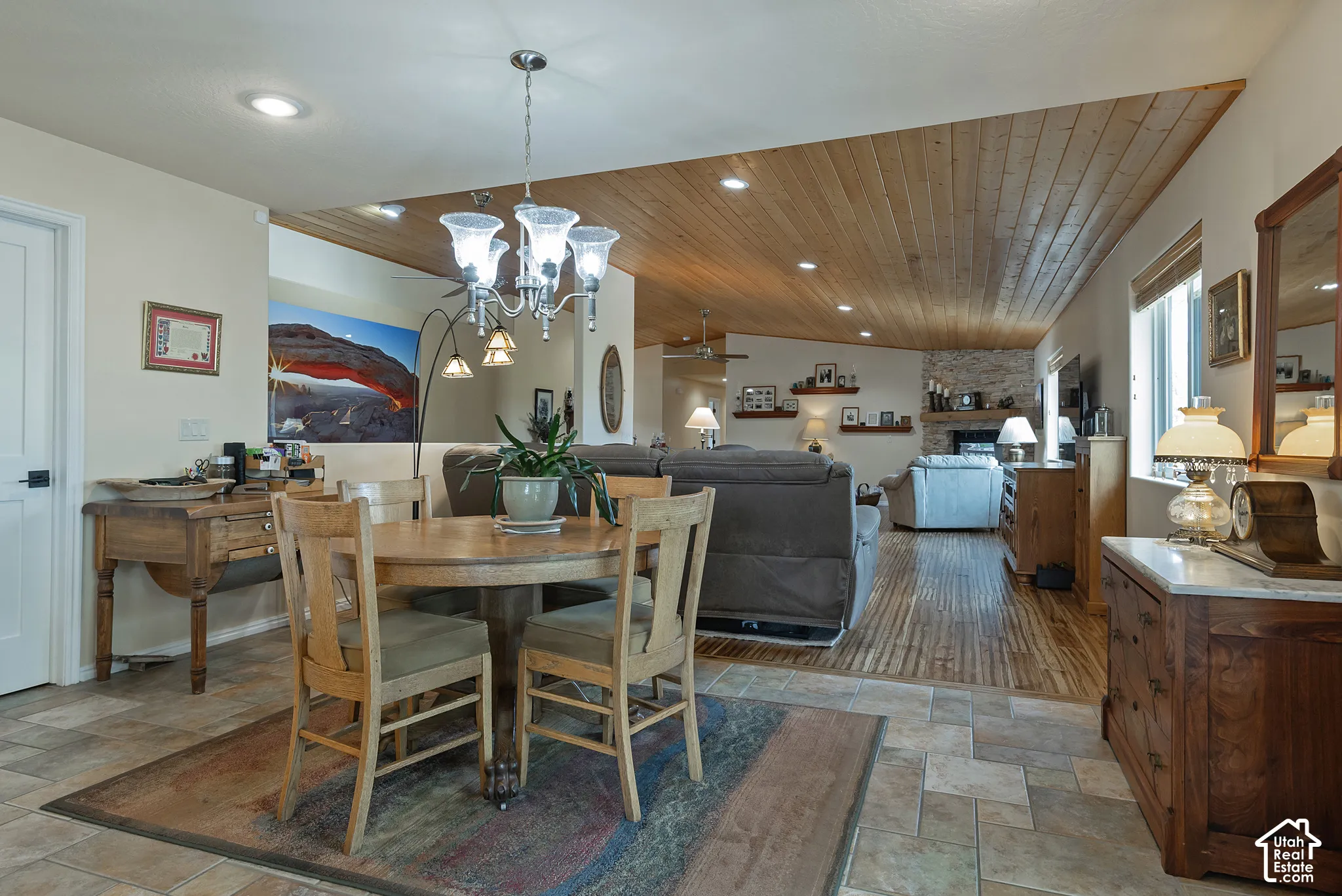 Tile flooring in dining area, wood-finish flooring in living area, wood-plank ceiling, recessed lighting, and stone fireplace surround