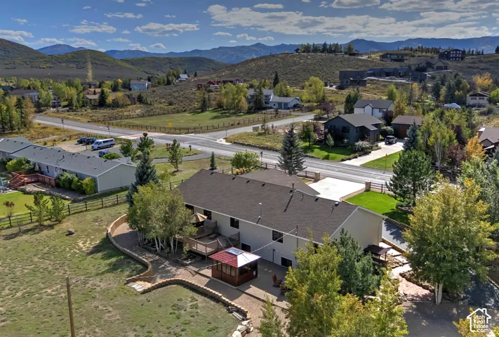Expansive lot with mountain backdrop, featuring a multi-level deck, a built-in fire pit, and a covered patio area
