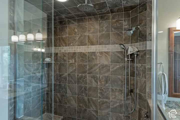 Glass-enclosed shower with a rainfall showerhead, handheld shower fixture, and tiled walls with a mosaic accent band