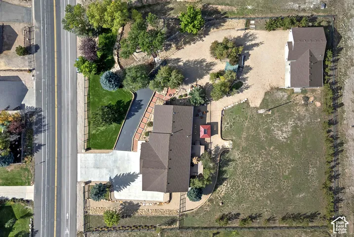 Expansive lot featuring a main residence, secondary detached structure, paved driveway, landscaped front yard with mature trees, and a large unmanicured rear yard