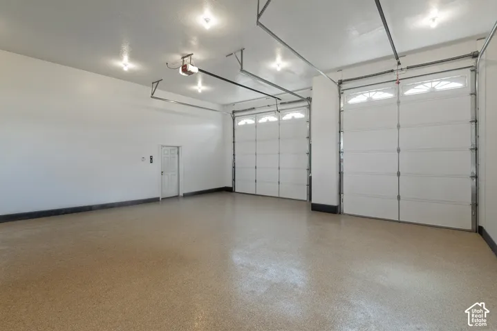 Spacious garage featuring two overhead doors, a pedestrian door, multiple ceiling-mounted light fixtures, and a durable epoxy-coated concrete floor
