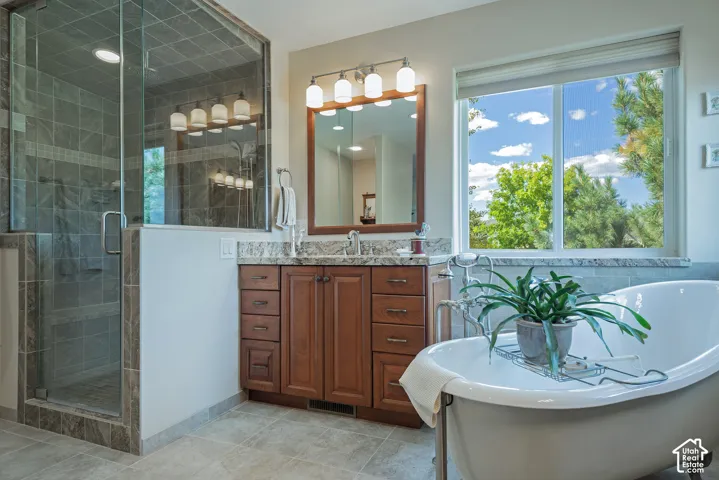 Walk-in shower with glass enclosure, freestanding soaking tub, wood-finish vanity with stone countertop, and large window