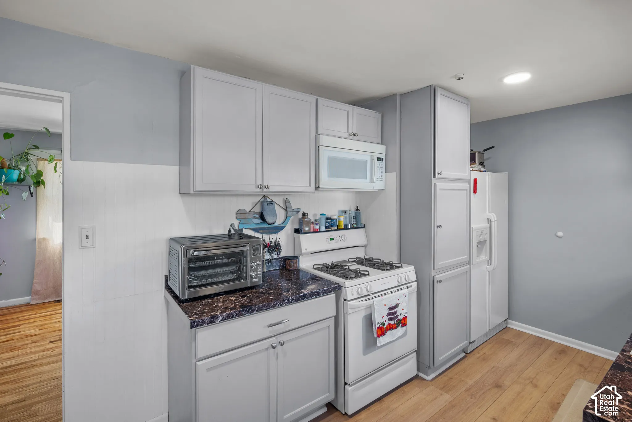 White cabinetry, laminate wood-finish flooring, white built-in microwave, white refrigerator