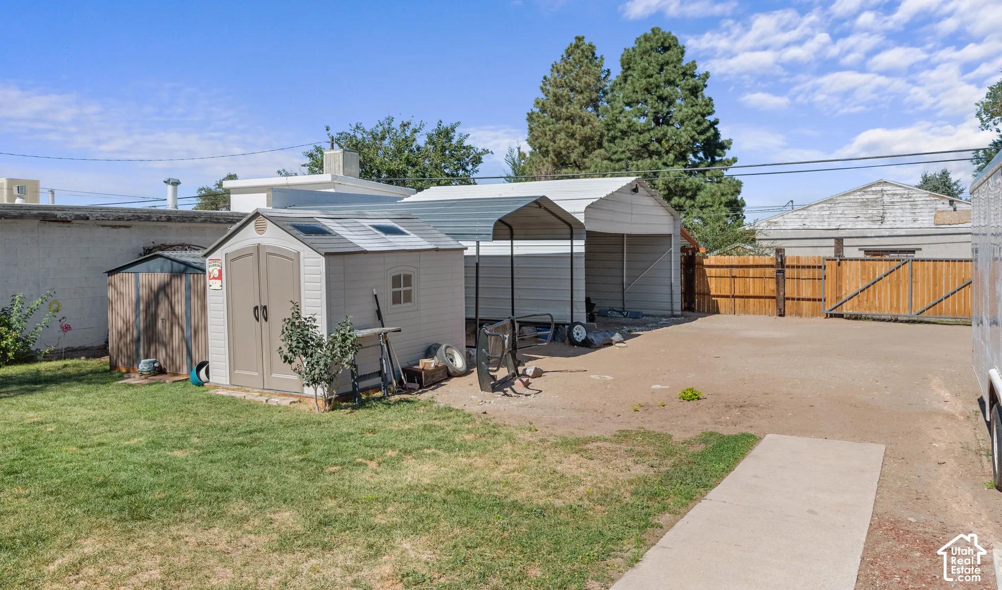 Expansive yard with grassy areas and concrete paths, featuring a storage shed, a covered carport, and a wood fence