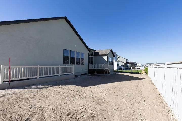 Stucco exterior with a pitched roof, multiple windows, a white privacy fence, and a wooden deck with railings