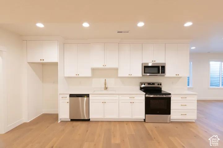 White cabinetry, stainless steel appliances, wood-finish flooring, recessed lighting, and a built-in microwave