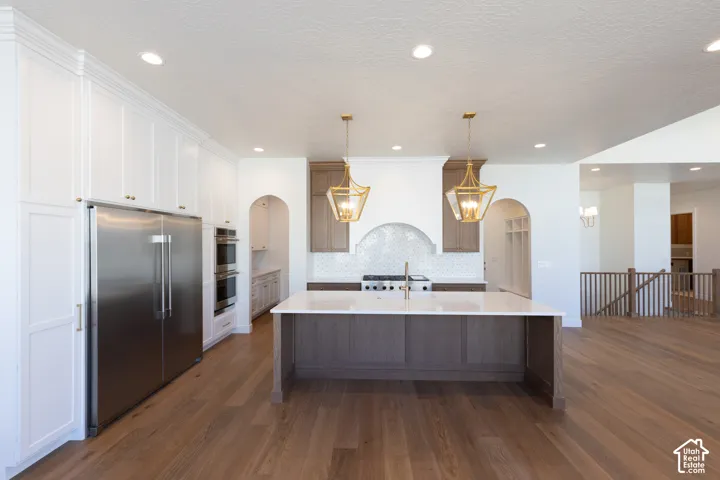 Gourmet kitchen with stainless steel appliances, spacious island with solid surface countertop, white and wood-finish cabinetry, and wood-finish flooring