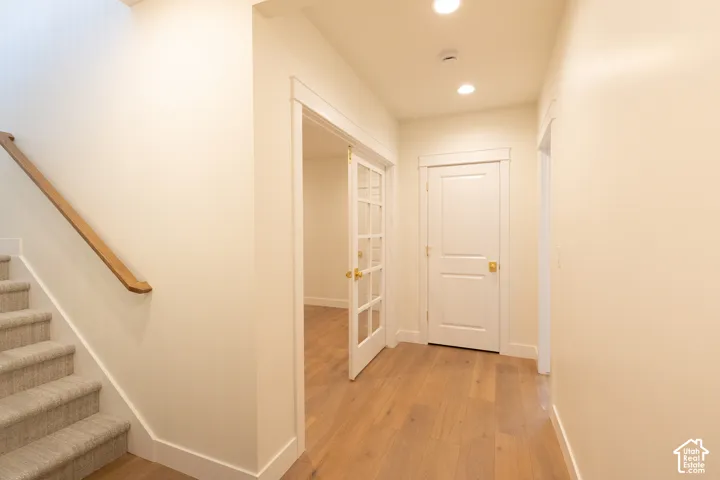Light wood-finish flooring, recessed ceiling lighting, light-toned walls, white trim, and a carpeted staircase with a wood handrail