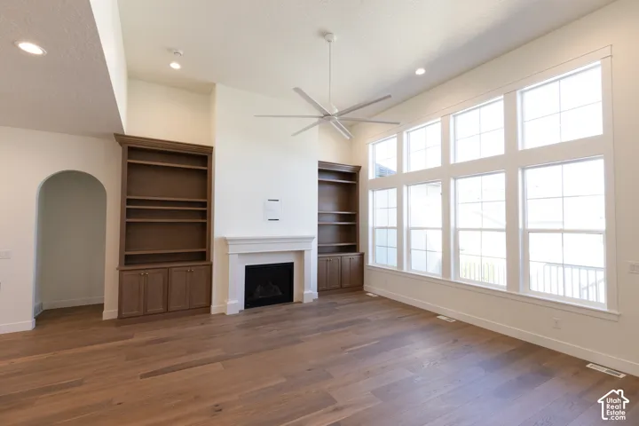 Wood-finish flooring, built-in shelving, white mantel fireplace, vaulted ceiling, and multi-pane windows