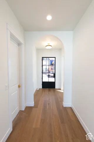 Wide plank wood-finish flooring, recessed ceiling lighting, arched entryway, and a black-framed glass door with shiplap wall accent