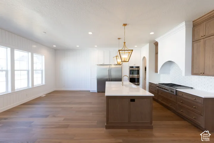 Gourmet kitchen featuring a large central island with quartz countertop, wood-finish flooring, stainless steel appliances, and custom cabinetry with brass hardware