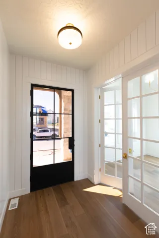 Wood-finish flooring, white shiplap wall paneling, a black-framed glass entry door, brass hardware, and a semi-flush mount ceiling light