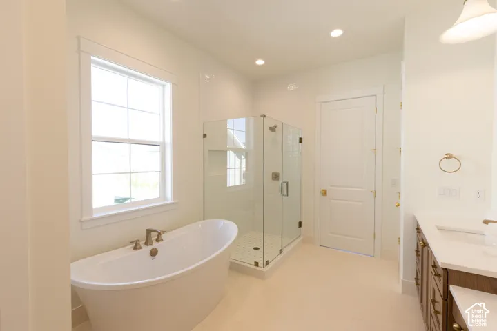 Freestanding soaking tub, glass-enclosed shower, dual-sink vanity with white countertop, and tiled flooring