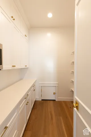 White cabinetry with gold-tone hardware, wood-finish flooring, recessed lighting, white countertops, and open shelving