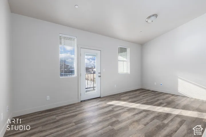 Wood-finish flooring, recessed ceiling lighting, a door with an integrated window, a metal balcony railing, and multiple windows with blinds