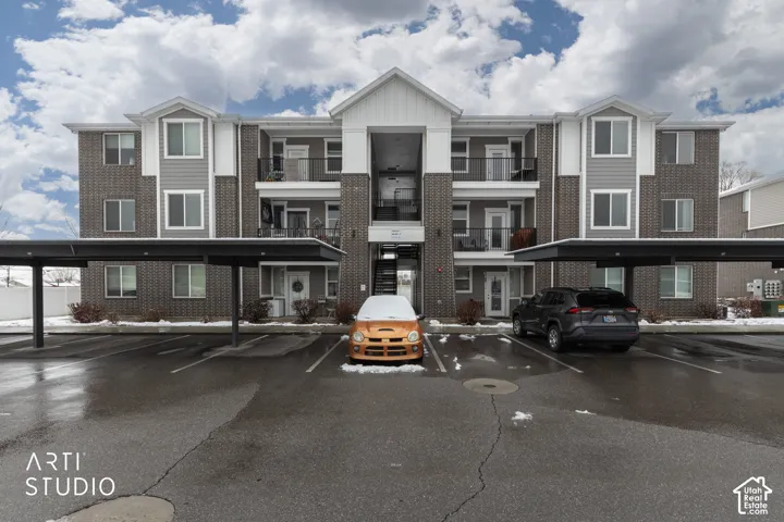 Multi-story building featuring brick and siding facade, multiple private balconies with black railings, and covered parking spaces