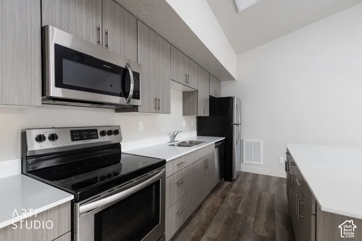 Kitchen featuring stainless steel appliances, wood-finish flooring, light-toned cabinetry, white countertops, and a double basin sink