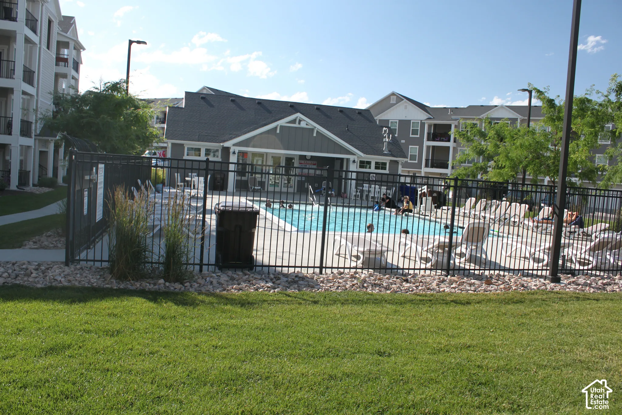 Outdoor swimming pool with a surrounding fence, concrete deck, and ample lounge seating