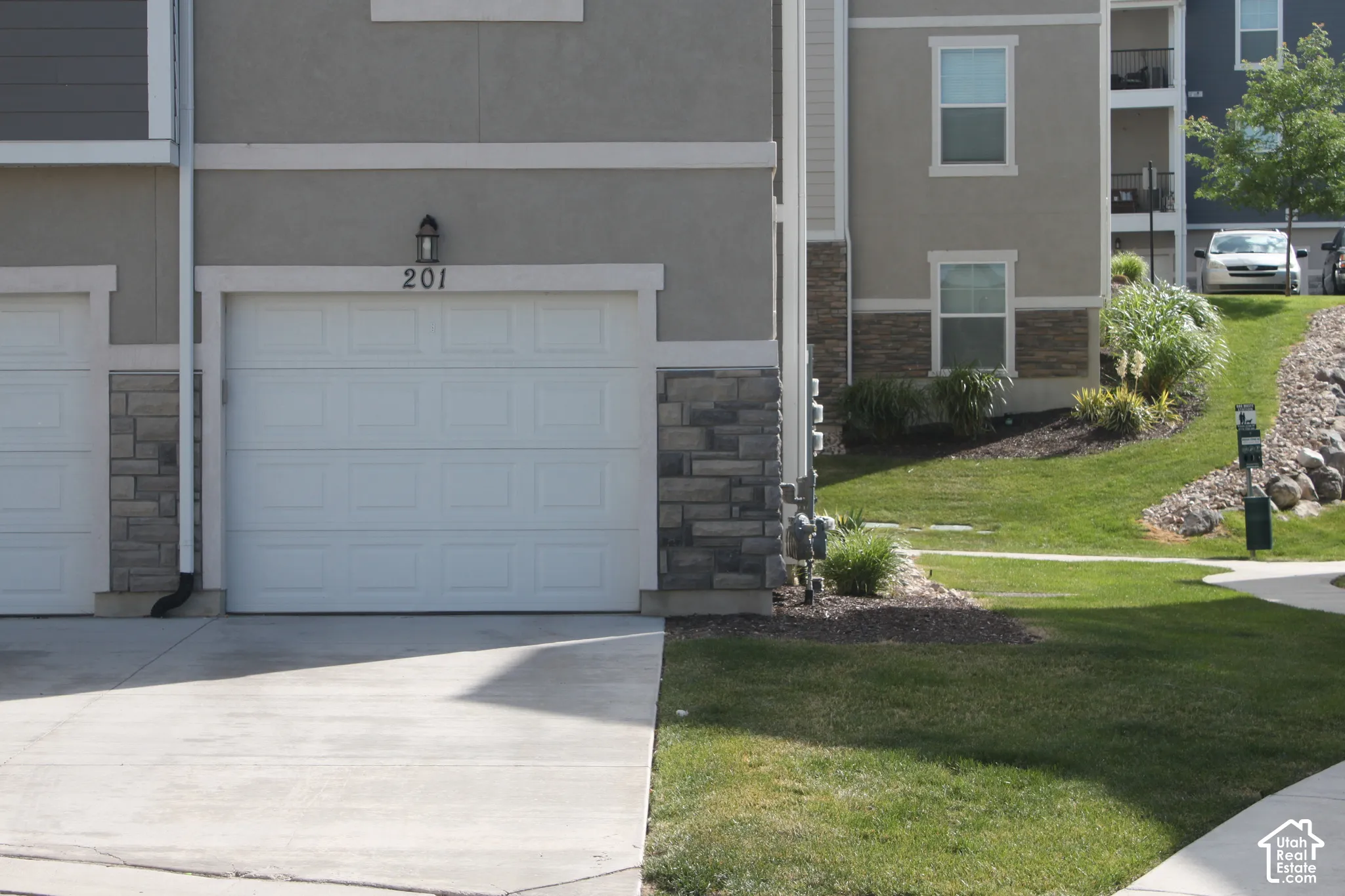 Attached garage with a white panel door, stone veneer accents, and stucco exterior
