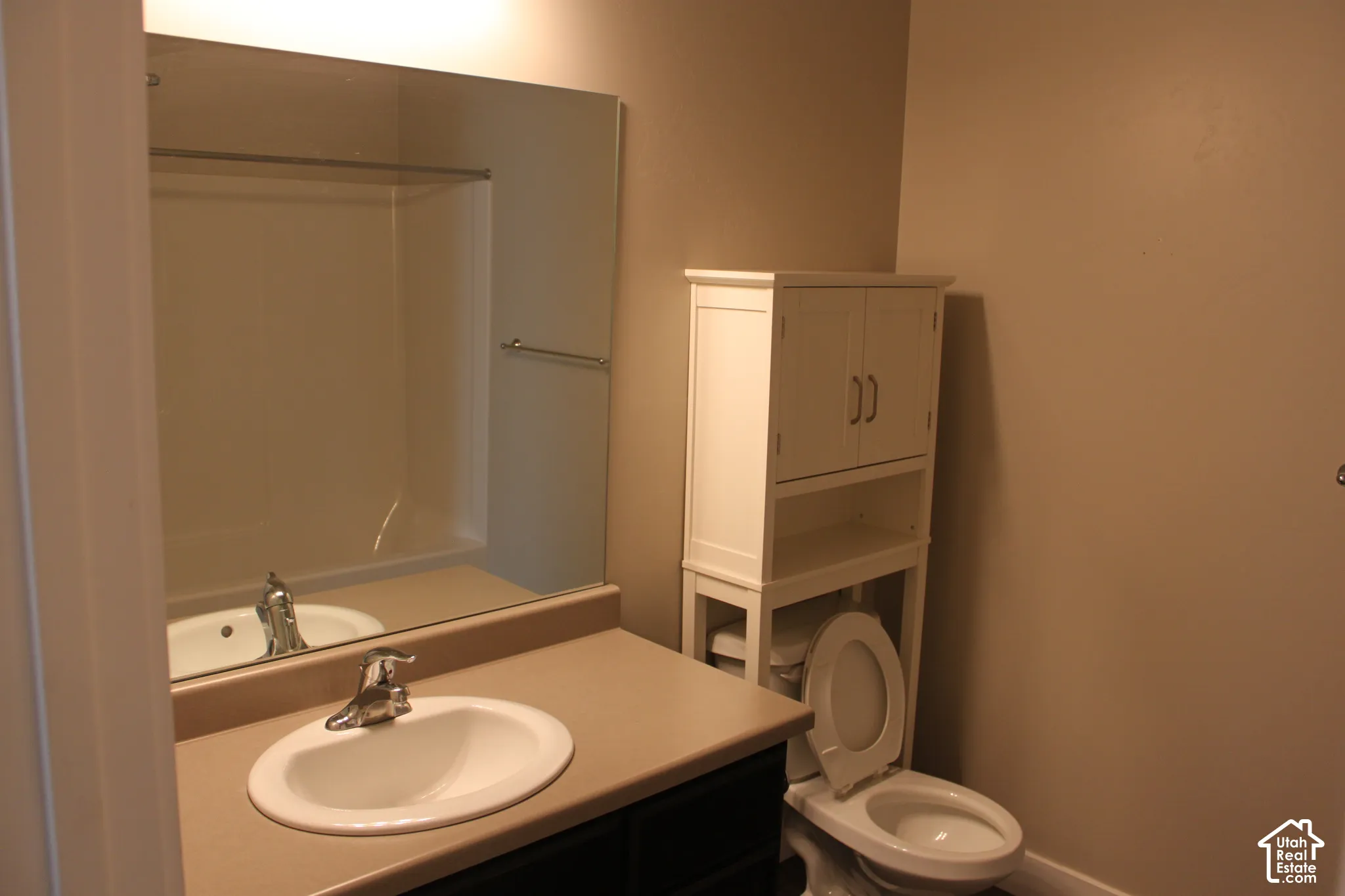 Hall bathroom featuring a full tub/shower, round undermount sink with single-handle faucet, laminate countertop, large framed mirror, toilet, and storage cabinetry with dual doors
