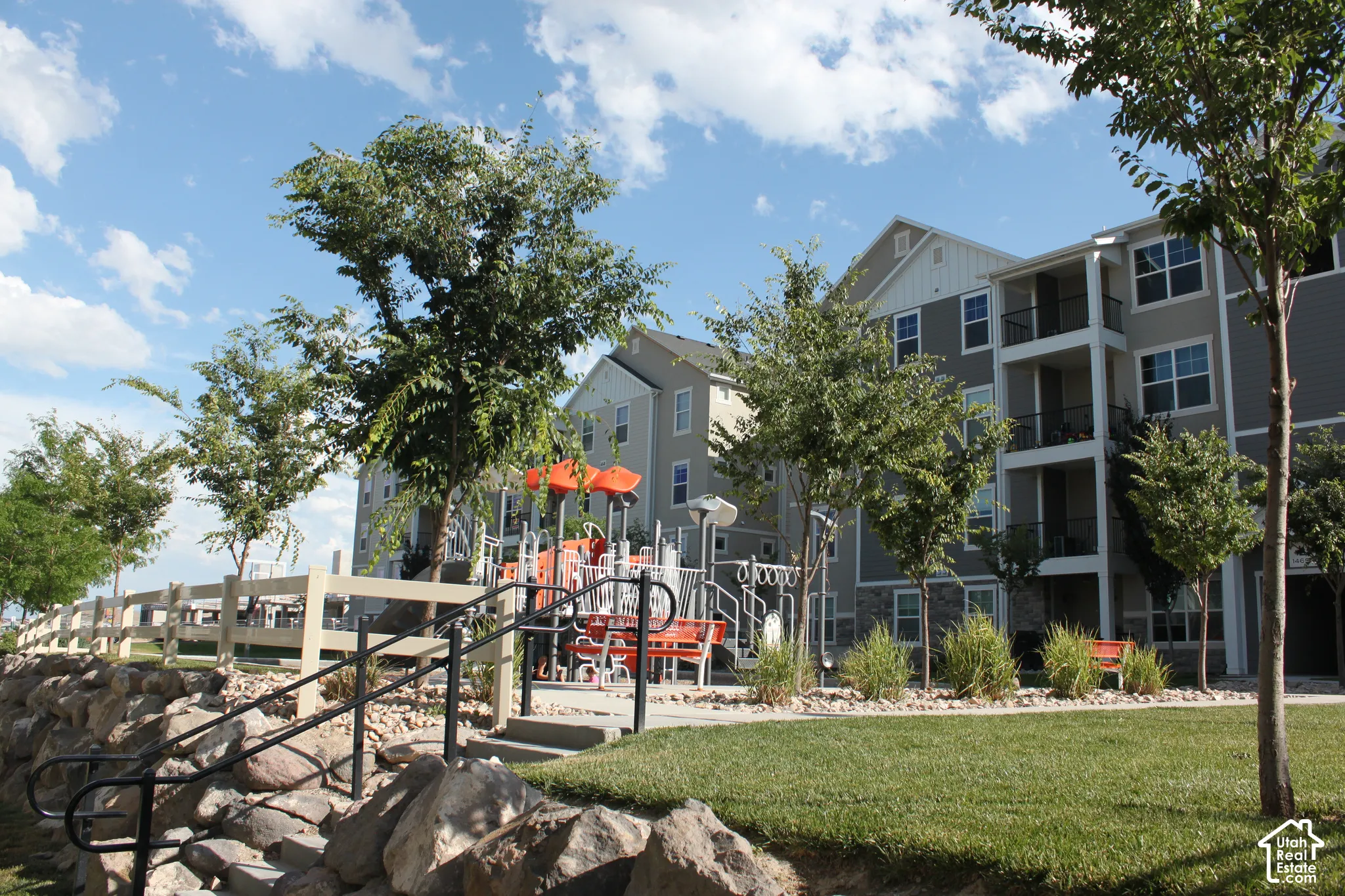 Expansive grounds featuring a manicured lawn, mature shade trees, and a multi-level playground structure with orange accents
