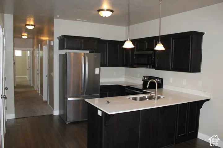 Kitchen featuring dark wood-finish cabinetry, light-toned quartz countertops, stainless steel appliances, and pendant lighting