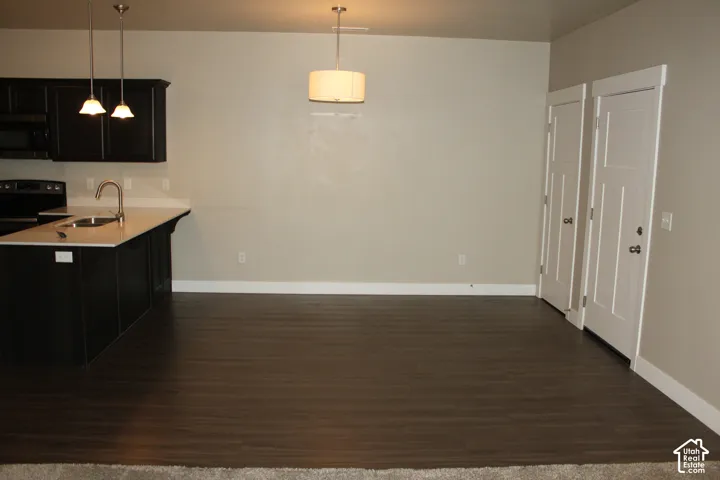 Kitchen island with a sink and a gooseneck faucet, dark wood-finish flooring, two pendant lights, and a drum-shade ceiling light looking from the family room