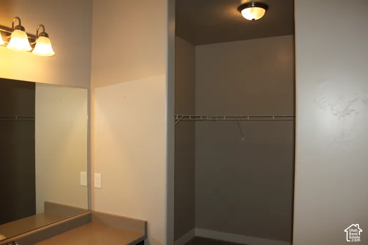 Built-in vanity counter with an integrated mirror, two-light fixture, and walk in closet area with a  shelf on suite to primary bedroom