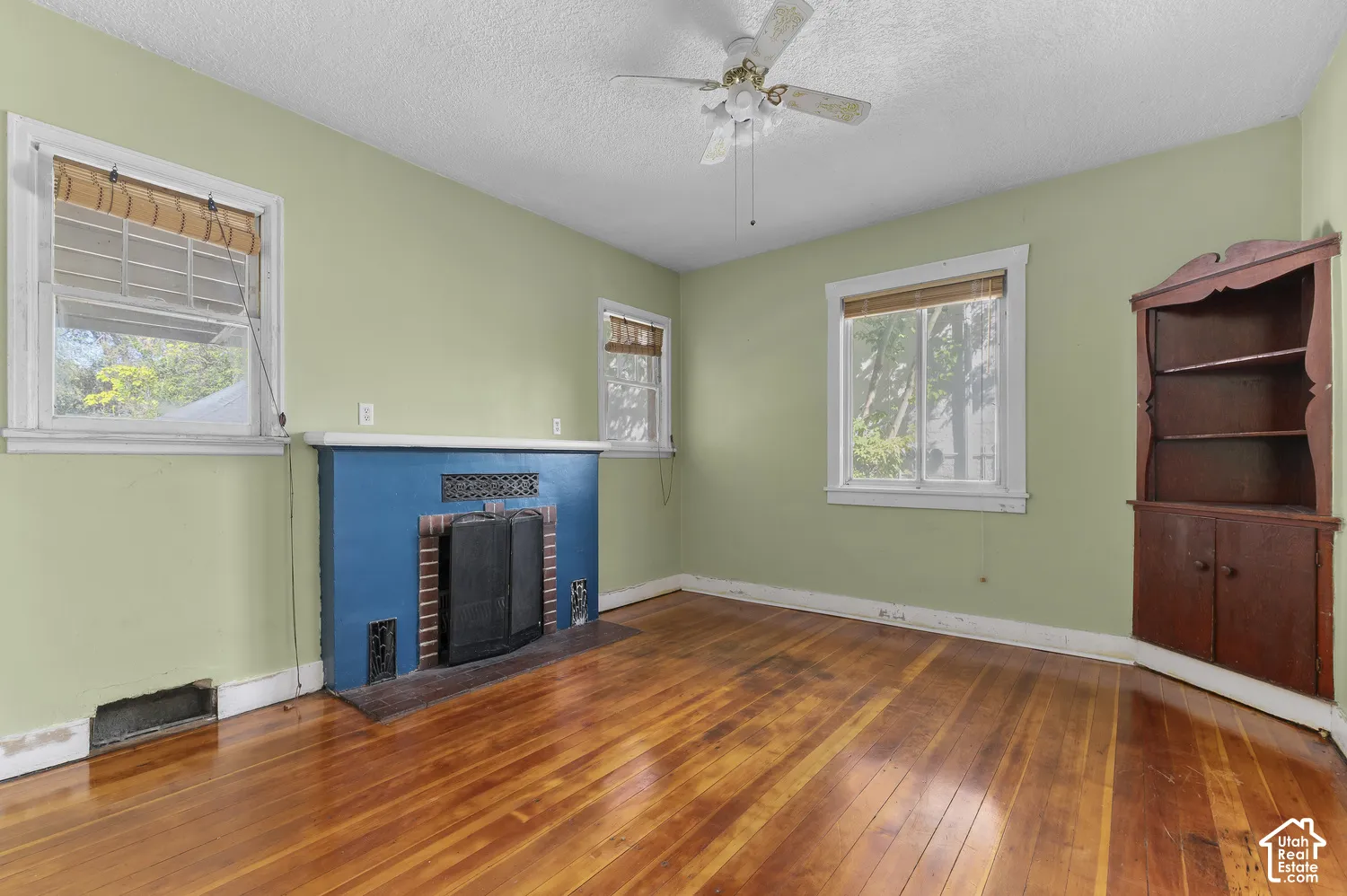 Wood-finish flooring, built-in corner cabinetry, a fireplace feature, and a ceiling fan