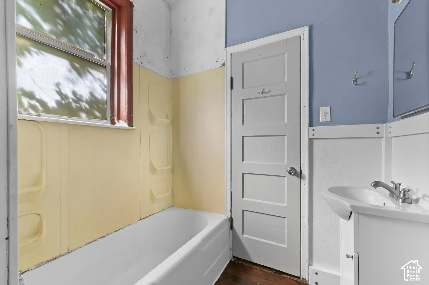 Built-in tub with a window, wall-mounted sink with a two-handle faucet, and white paneled wainscoting