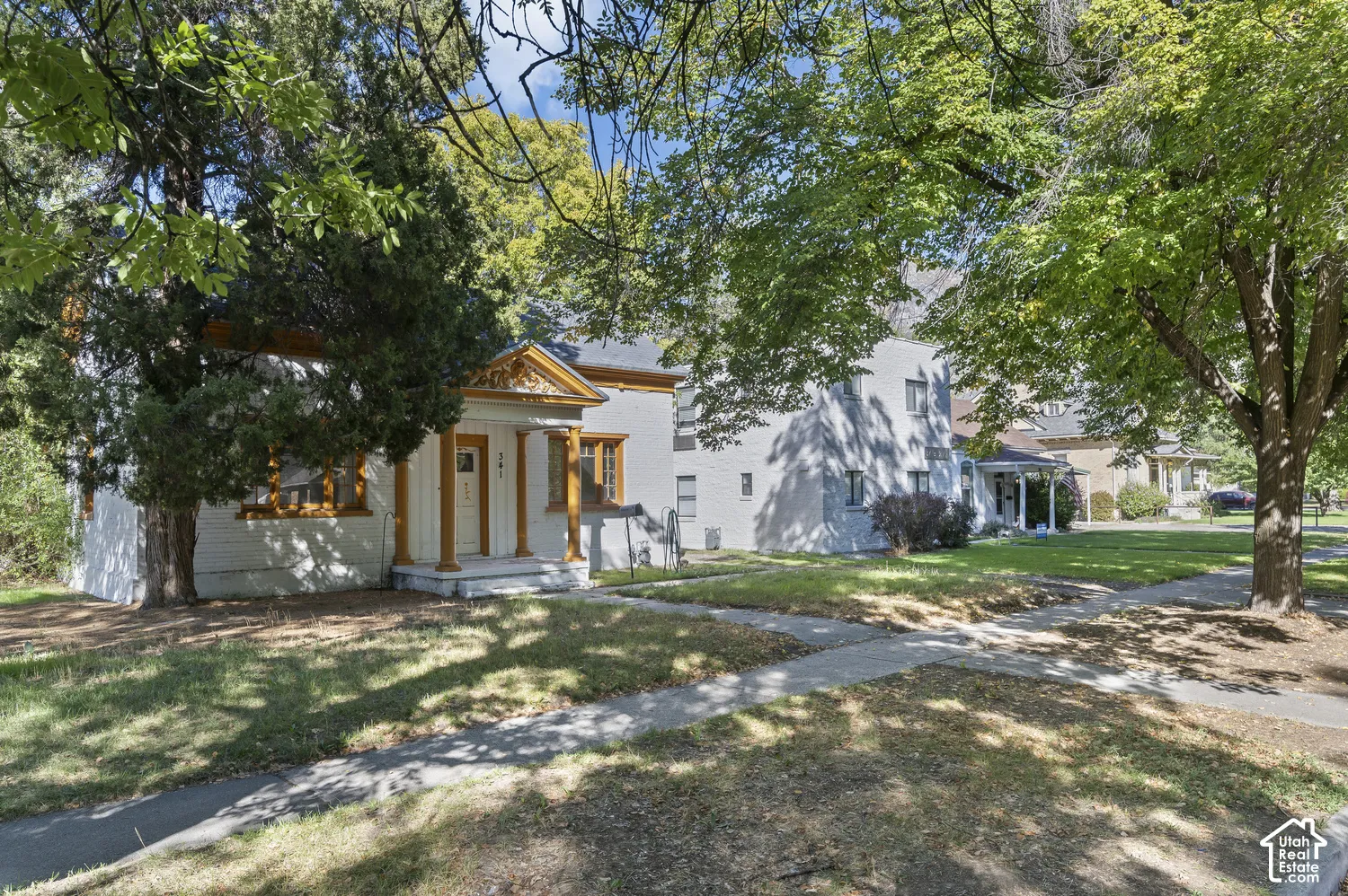 White exterior with decorative yellow trim, a front porch with columns, a white front door, and mature trees providing shade