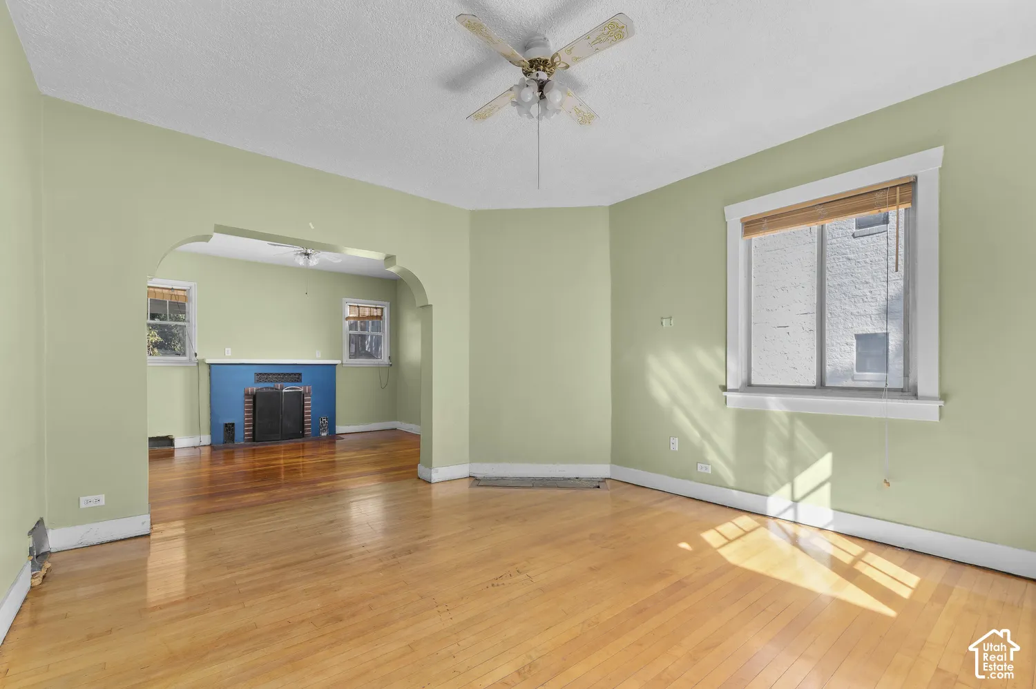 Hardwood flooring throughout, arched doorway, ceiling fan, and multiple windows