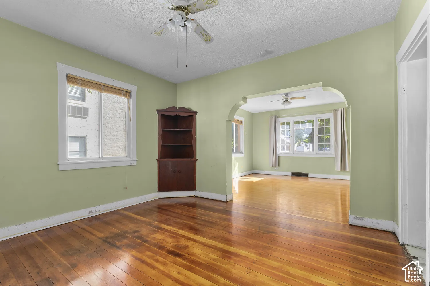 Hardwood flooring throughout, multiple windows with natural light, integrated corner shelving, and an arched doorway