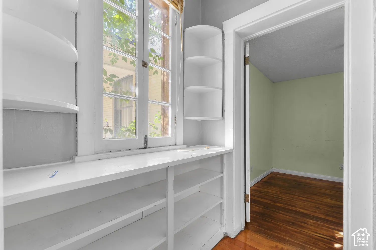 Built-in shelving, corner shelving, wood-frame window, and a separate room with wood-finish flooring
