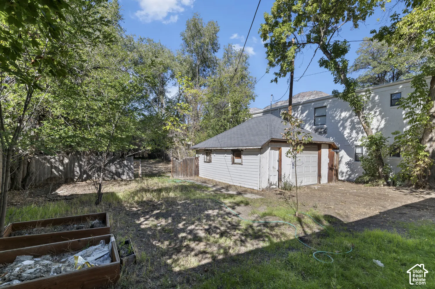 Detached garage with a shingled roof, a fenced perimeter, mature trees, and a raised planter box