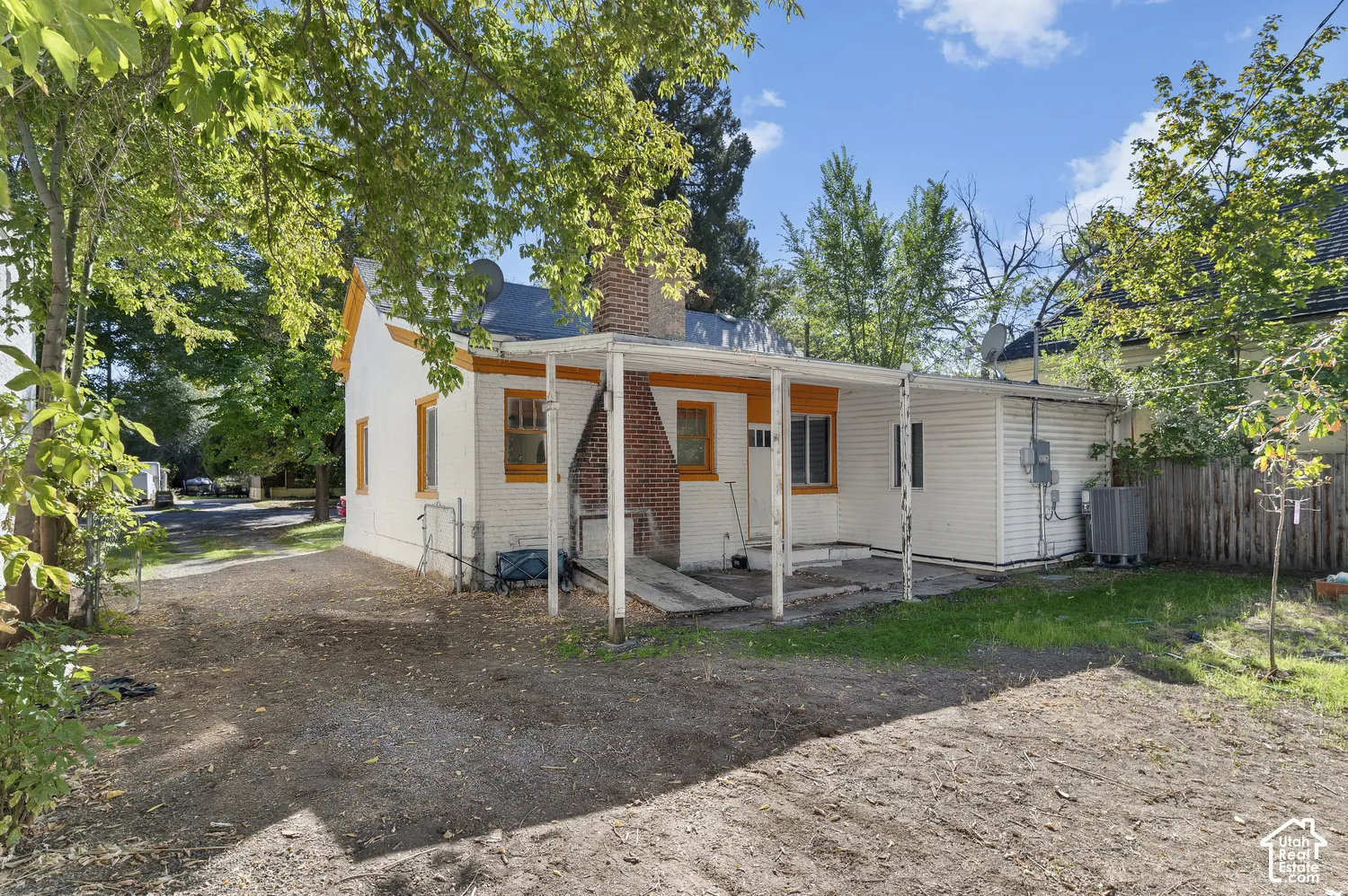 White exterior featuring orange trim, a brick chimney, and a covered patio