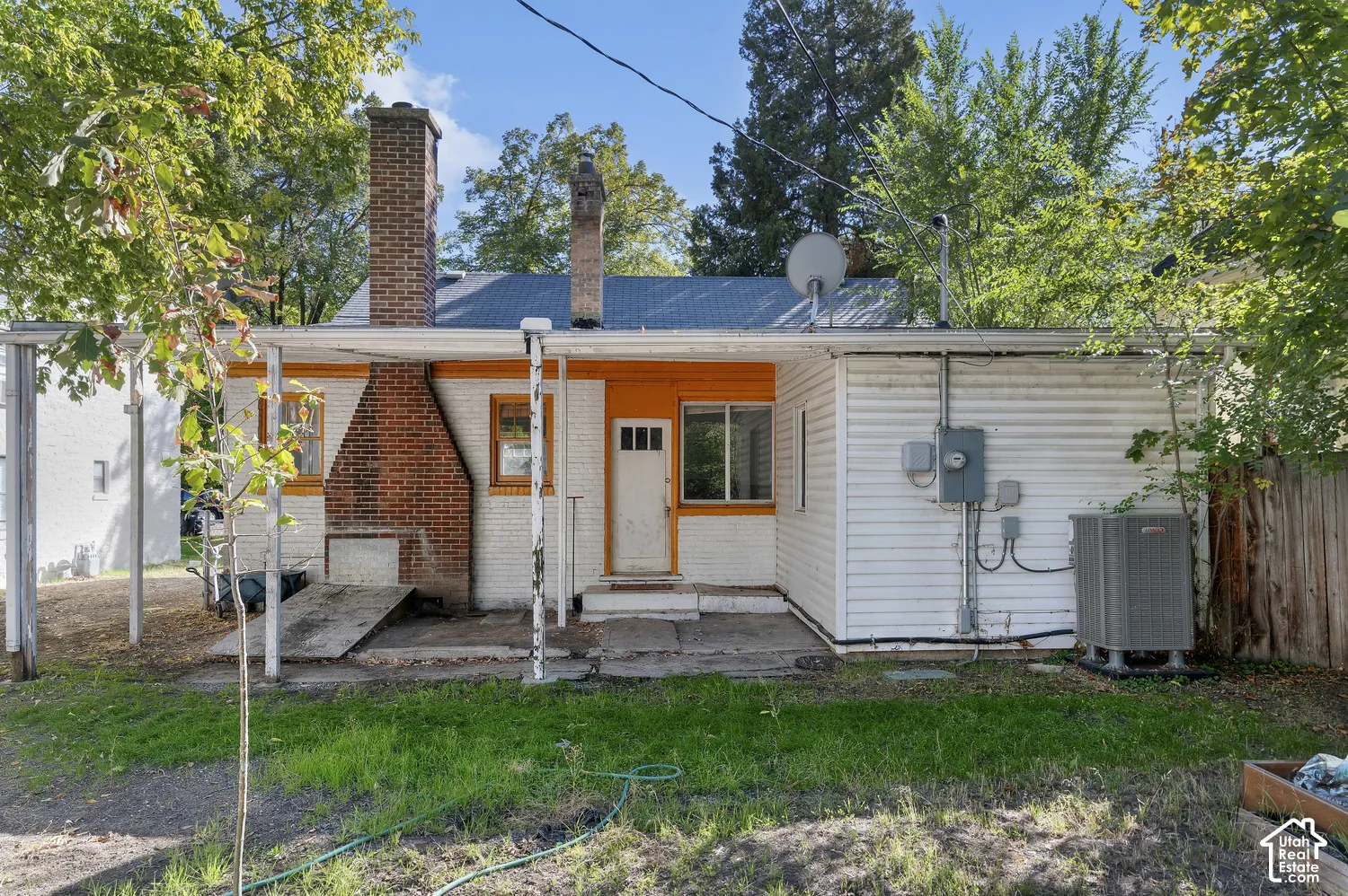 Rear exterior featuring white siding with orange trim, a prominent brick chimney, and a concrete patio