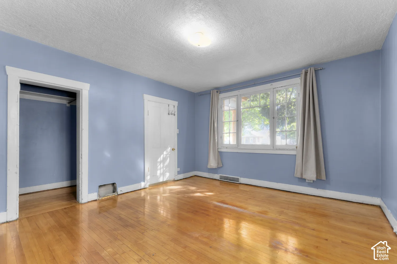 Hardwood flooring, painted walls, overhead lighting, window with white trim, and a storage alcove