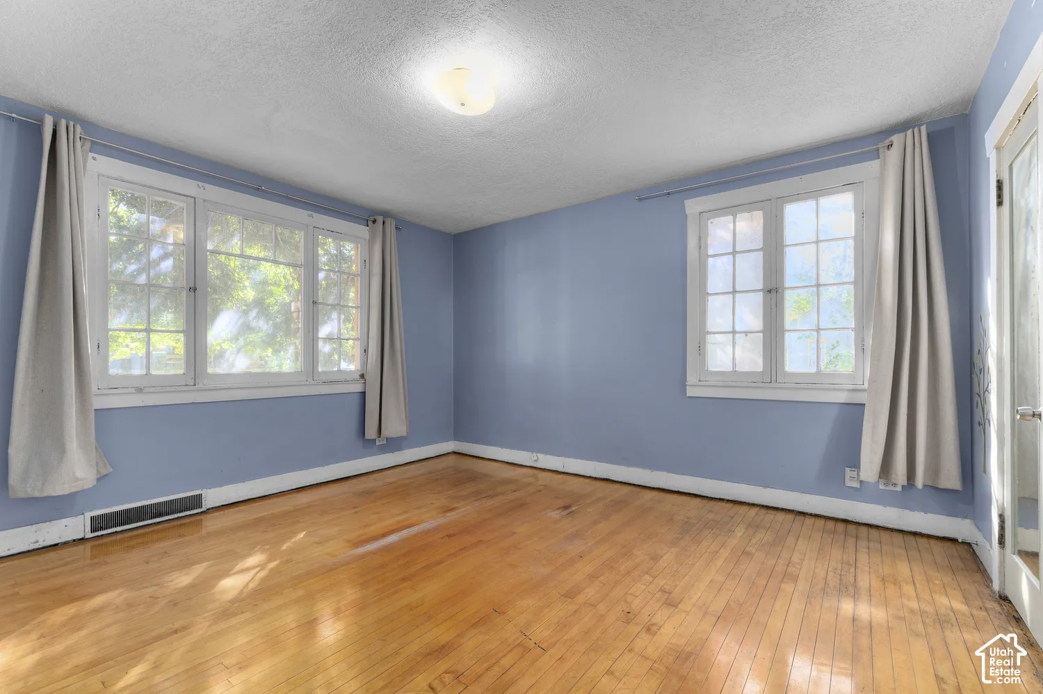Hardwood flooring, multiple windows, overhead flush-mount lighting, and light blue wall finish