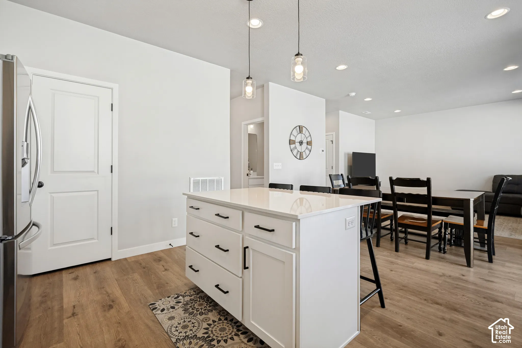 Kitchen island with a light-toned countertop, wood-finish flooring, recessed lighting, and pendant lighting fixtures