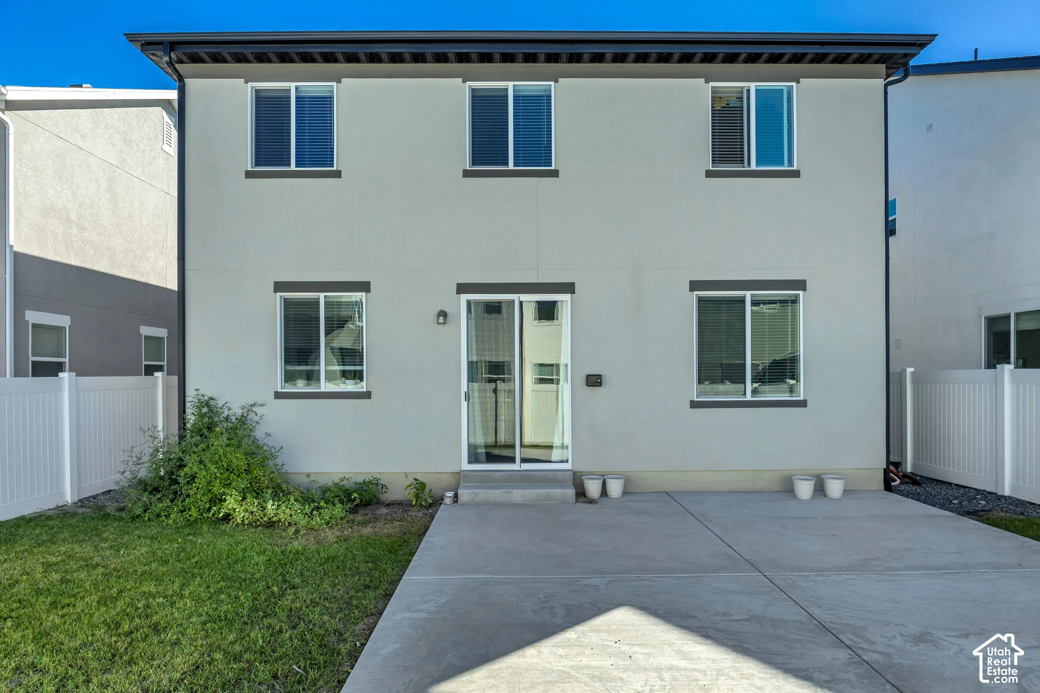 Stucco exterior featuring multiple windows with dark trim, a sliding glass door, and a concrete patio