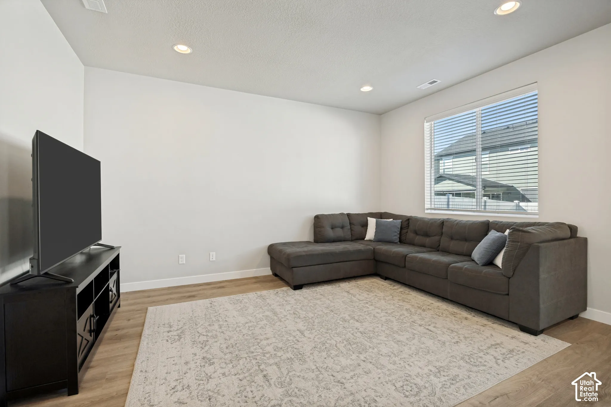 Recessed ceiling lighting, light wood-finish flooring, and a large window with blinds