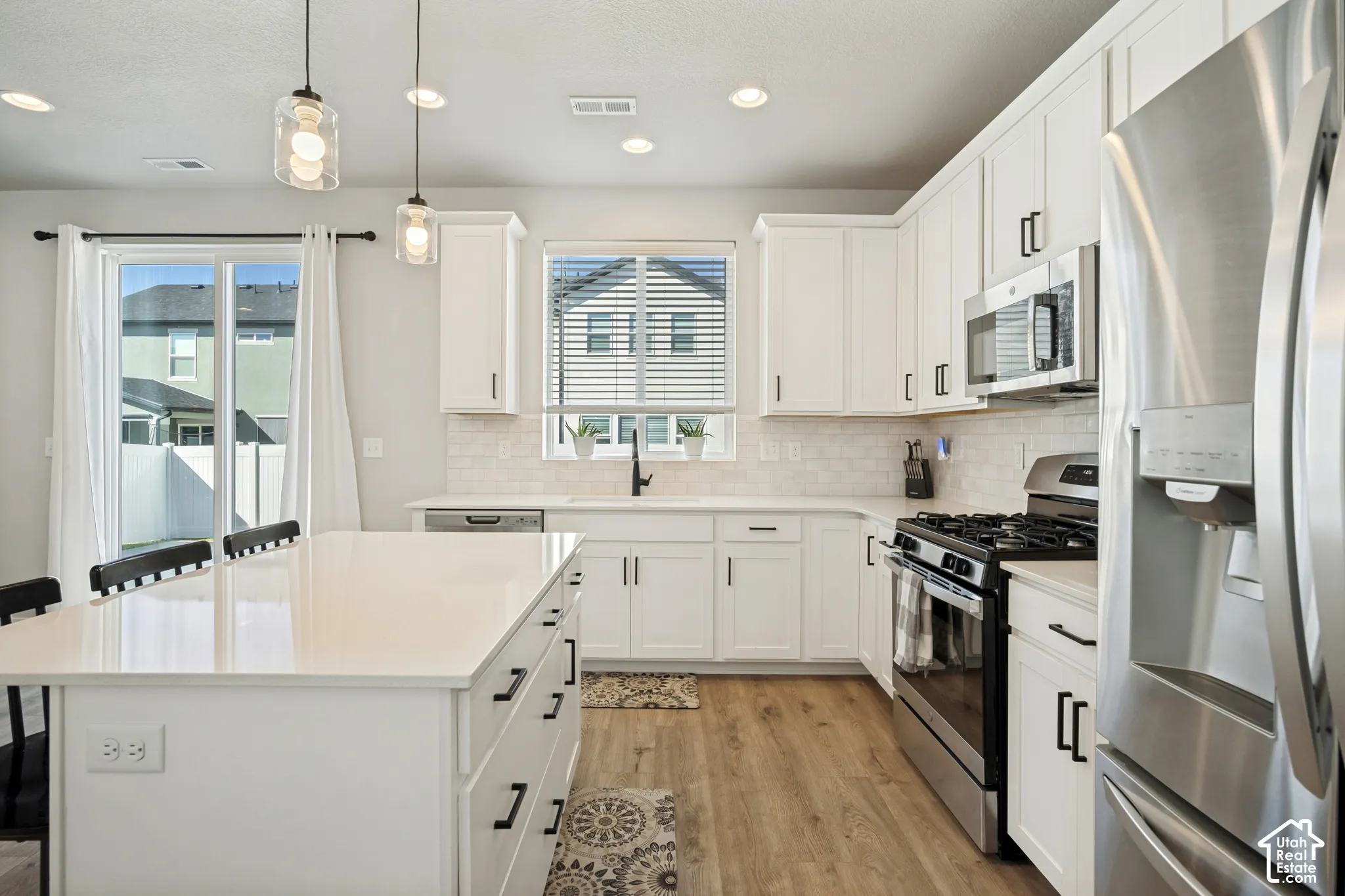 White cabinetry kitchen featuring a center island with light-toned countertop, stainless steel appliances, wood-finish flooring, and a sliding glass door