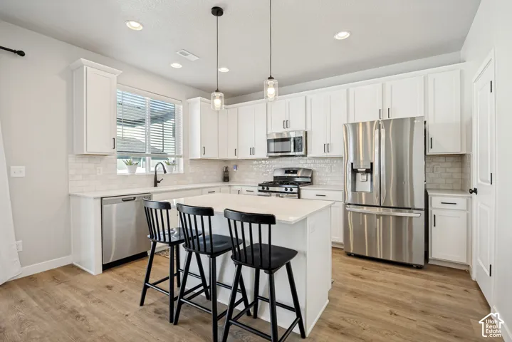 White cabinetry, stainless steel appliances, central island, wood-finish flooring, and recessed lighting