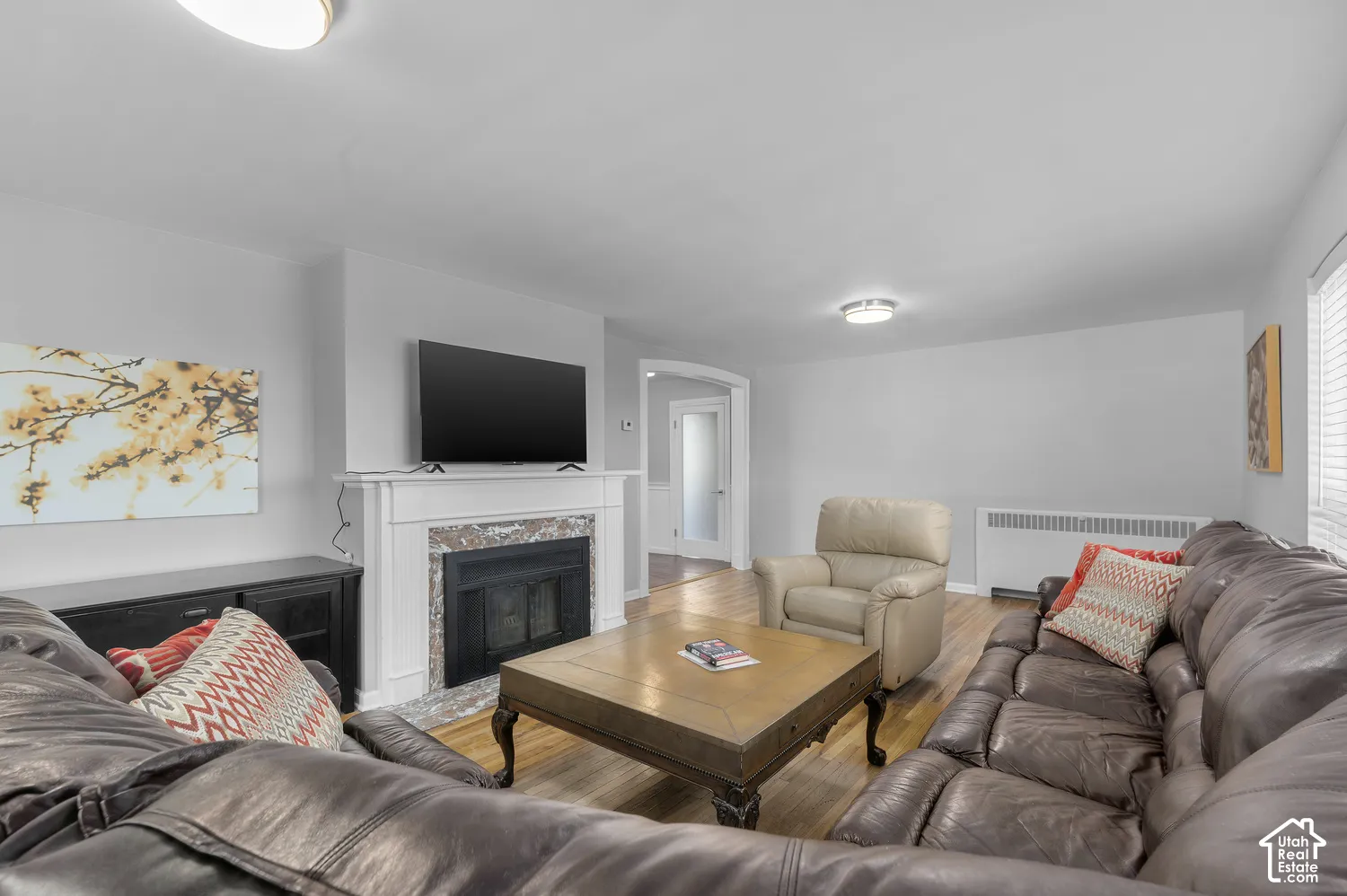 Wood-finish flooring, white fireplace mantel with stone surround, archway entry, and ceiling-mounted light fixtures