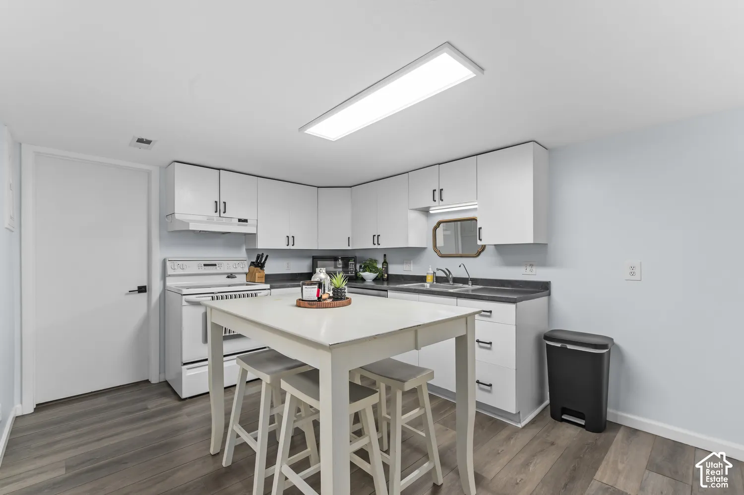 Updated kitchen with white cabinetry, dark countertops, and wood-finish flooring